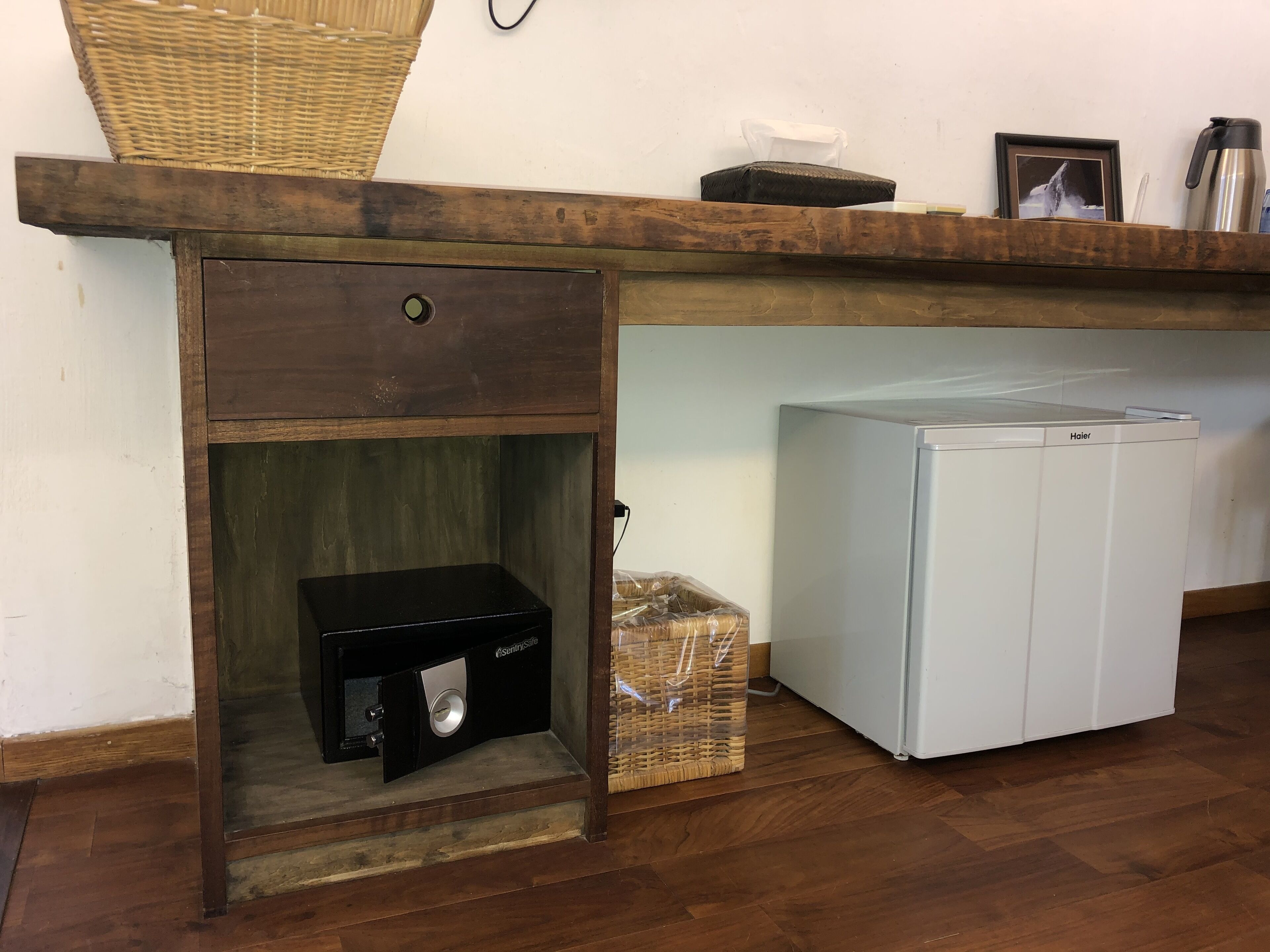A compact kitchen area with a wooden countertop, a small refrigerator, a safe, and a basket.