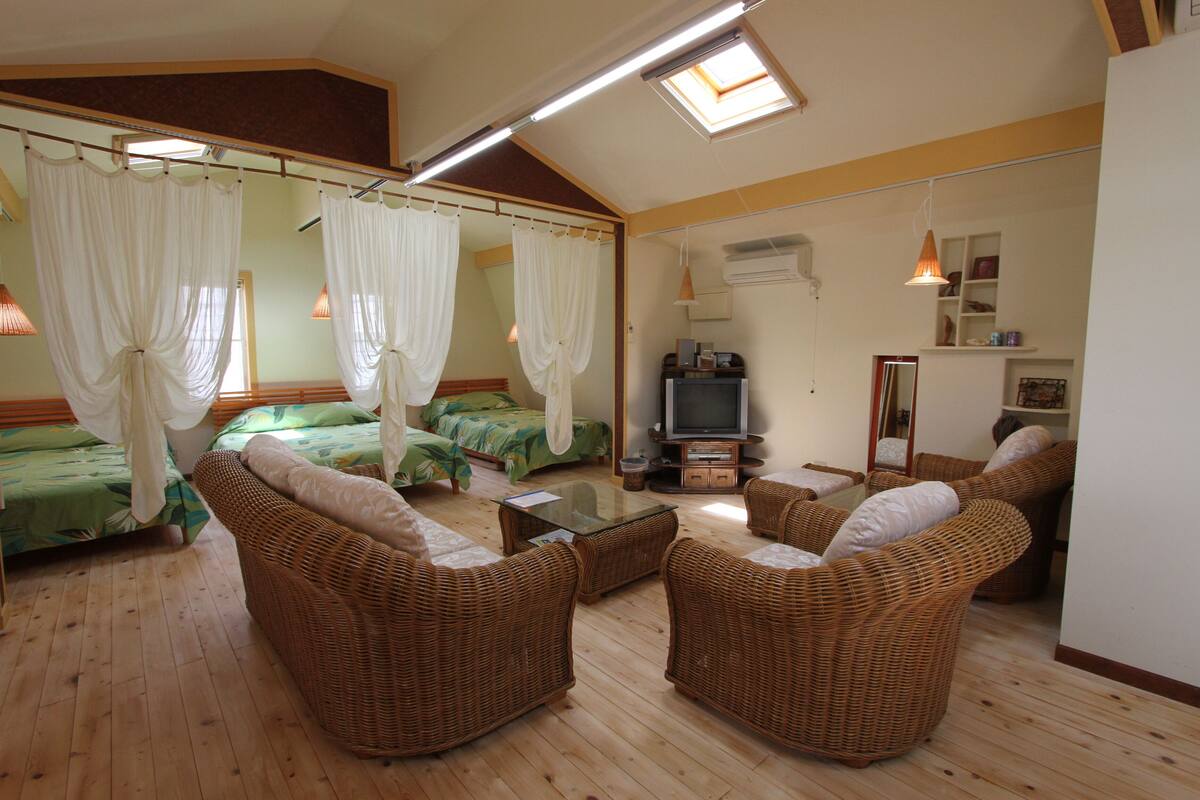 Ein Zimmer mit zwei Betten, einem Fernseher, Korbmöbeln und einem Deckenventilator.