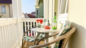 Een balkon met rieten meubilair, een tafel met een fles en een schaal fruit.