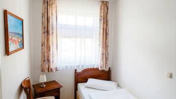 Una camera da letto con un letto, un comodino, una sedia, un quadro e una finestra con tende.