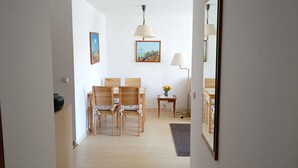 A room with a wooden dining table and chairs, a small side table with a lamp, and a painting on the wall.