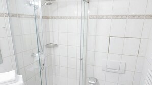Een badkamer met een douchecabine van glas, witte tegels, een toilet en een wastafel.