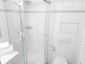 A bathroom with a glass-enclosed shower, white tiles, a toilet, and a sink. - Apartment Rosenhof 04 - Wh. 04 (Kühlungsborn)