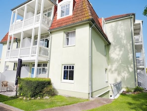 Un edificio residencial de varios pisos con balcones, un jardín y un camino que lleva a la entrada.