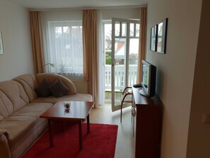 A living room with a sofa, a coffee table, a TV on a stand, and a sliding glass door leading to a balcony. - Apartment Rosenhof 04 - Wh. 04 (Kühlungsborn)