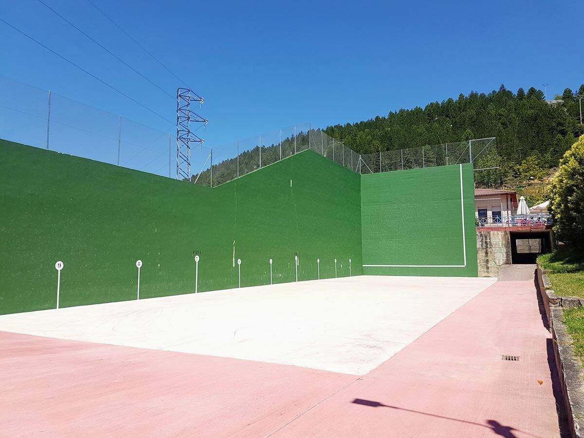 A tennis court with a green and white surface, surrounded by a fence, with a clear sky and trees in the background.