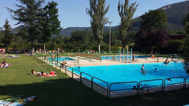 Una piscina con múltiples carriles, rodeada de césped y árboles.
