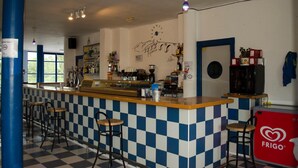 Zona de bar con suelo a cuadros, barra, taburetes y un refrigerador marca 'FRIGO'.
