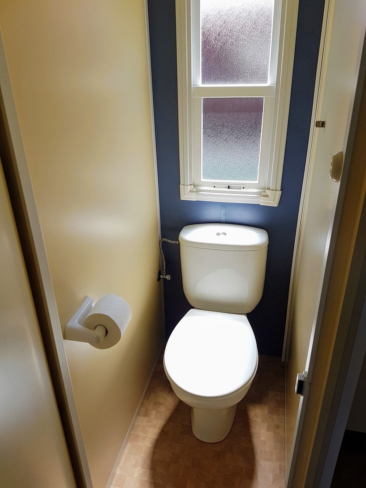 Un baño pequeño con inodoro, ventana y un rollo de papel higiénico.