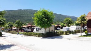 Un camping con vehículos recreativos y cabañas, rodeado de árboles y montañas.