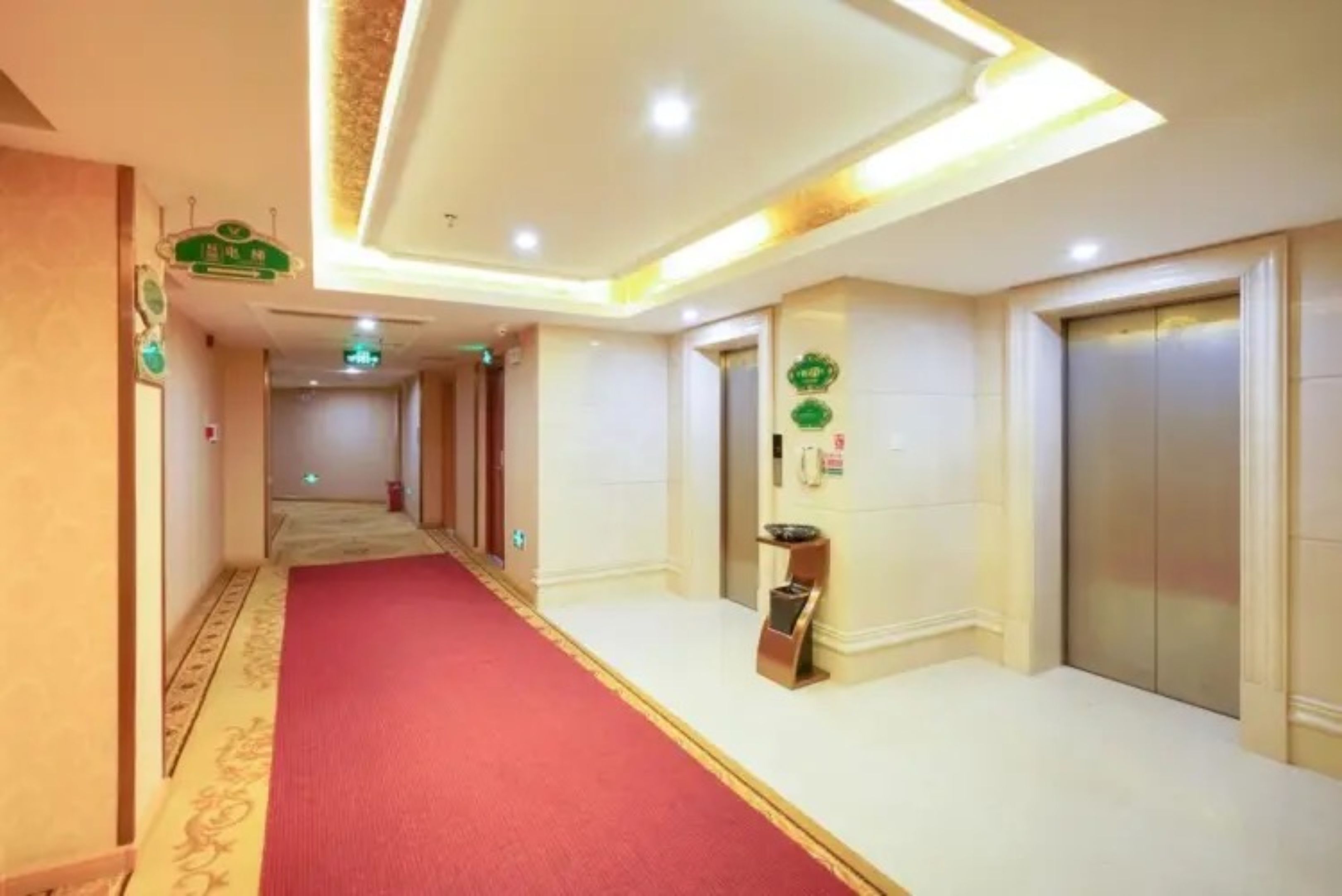 A hotel corridor with a red carpet, elevators, and a reception area.