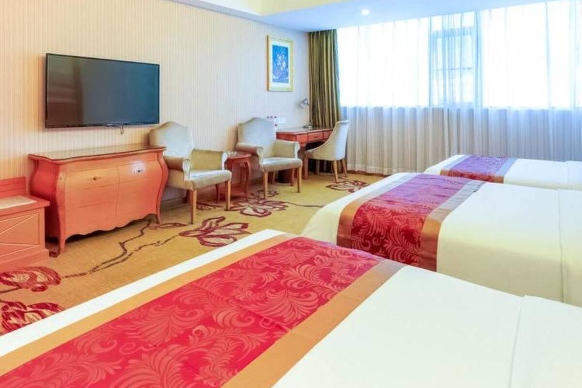 A hotel room with two beds, a desk, a chair, a television, and a window with curtains.