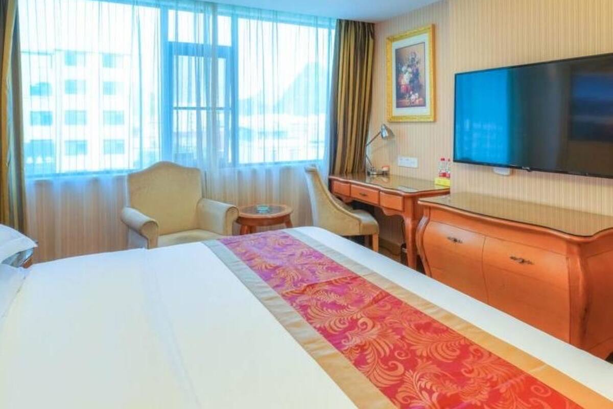 A hotel room with a large bed, a desk, a chair, a television, and a window with curtains.