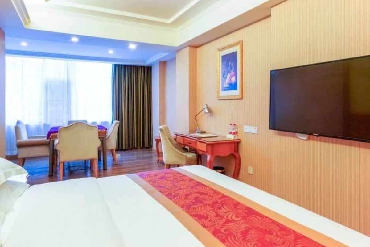 A hotel room with a bed, a desk, a chair, a television, and a window with curtains.