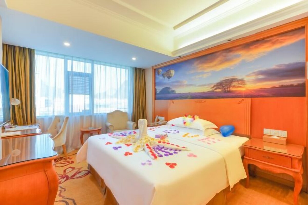 A hotel room with a large bed, a desk, a chair, and a nightstand.