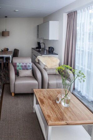 Una sala de estar moderna con un sofá, una mesa de centro de madera y una zona de cocina con armarios y un hervidor.