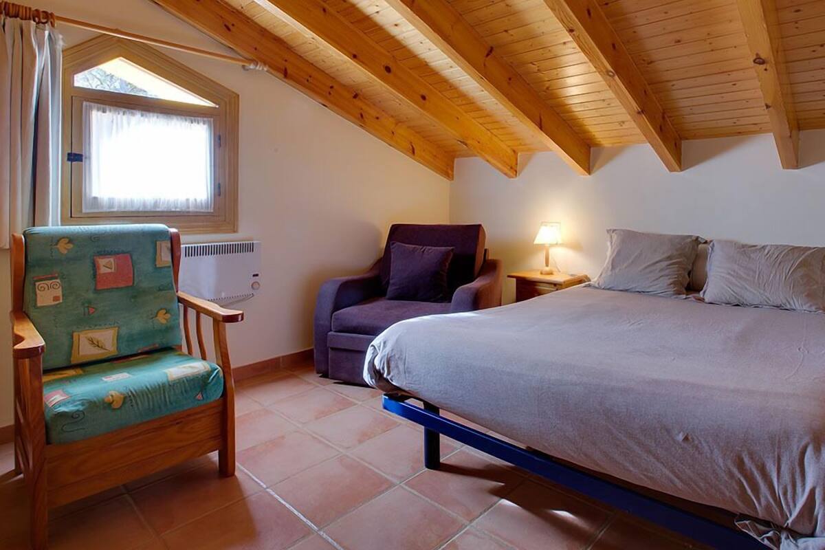 A bedroom with a bed, a chair, a window, and a lamp.