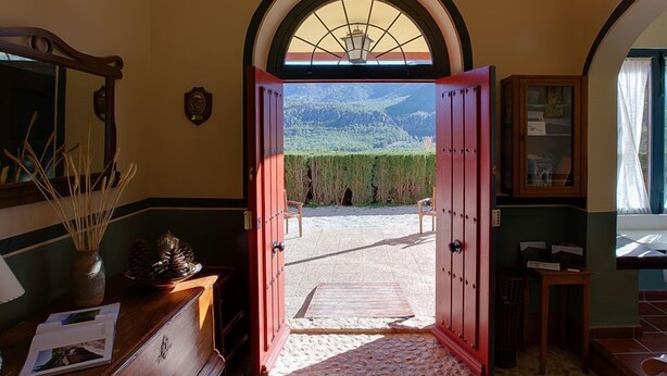 Habitació amb escriptori de fusta, mirall i vista a un paisatge de muntanyes a través d'una porta oberta.