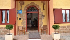 Entrada d'hotel amb arc de pedra, caires de fusta i plantes en testos.