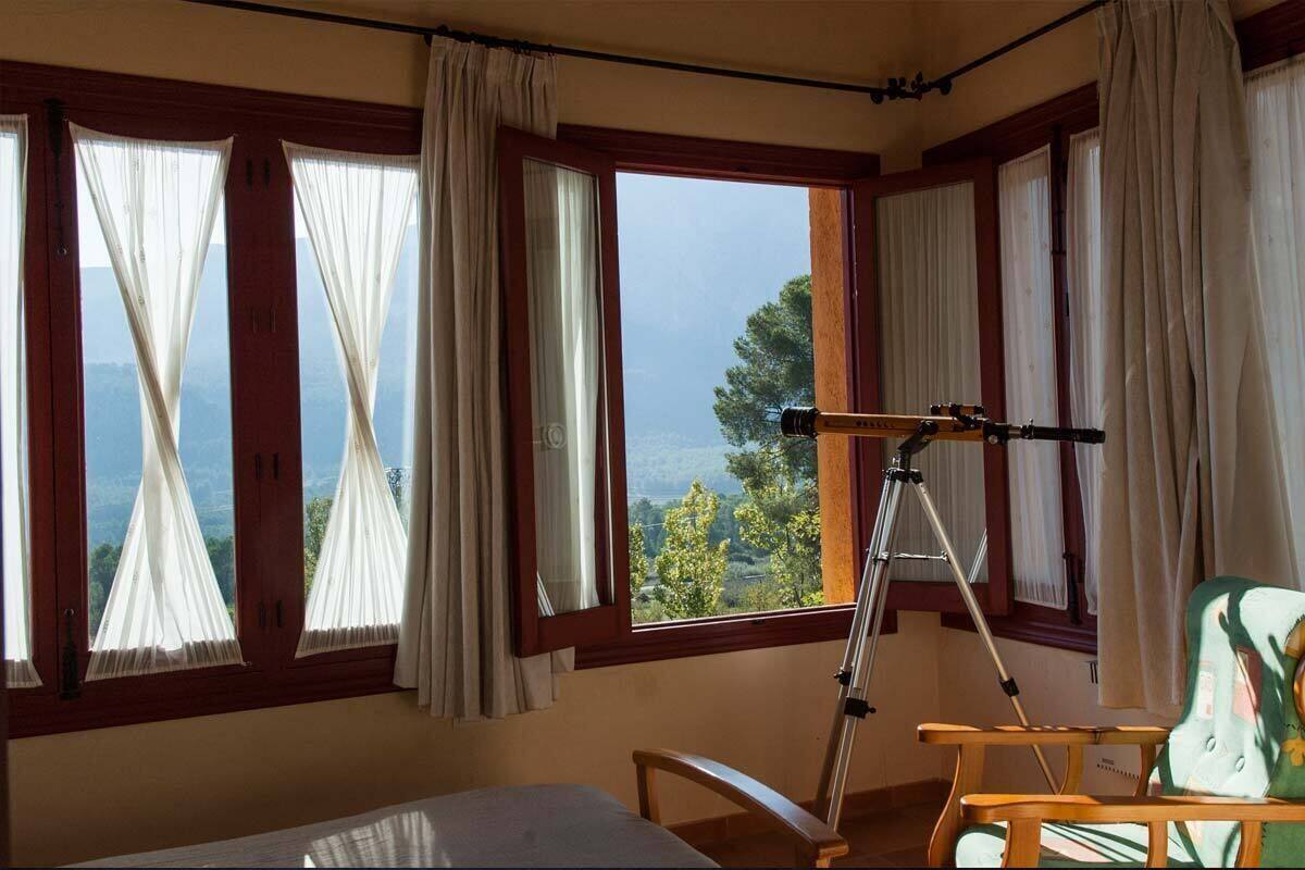A room with large windows, a telescope, and a chair.
