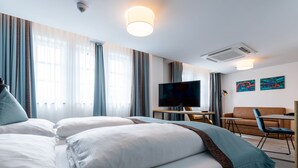 A hotel room with a bed, a TV, a desk, and a sofa. - Trip Inn Living & Suites (Essen)