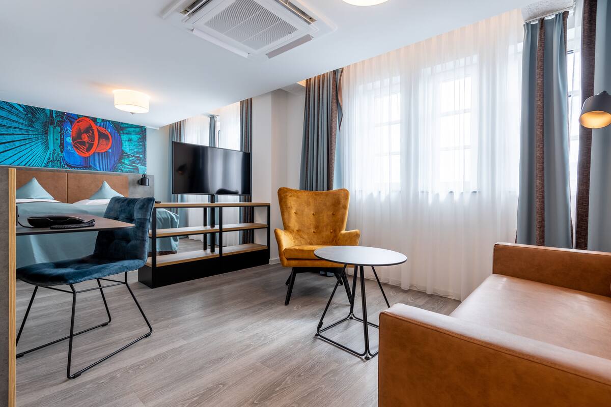 Une chambre d’hôtel moderne, équipée d’un lit, d’un bureau, d’une chaise, d’un canapé, d’une télévision et d’un tableau au mur.