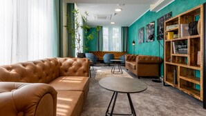A modern lounge area with leather sofas, a round table, and a wooden bookshelf. - Trip Inn Living & Suites (Essen)
