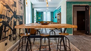 A modern dining area with a large wooden table, bar stools, and pendant lighting. - Trip Inn Living & Suites (Essen)