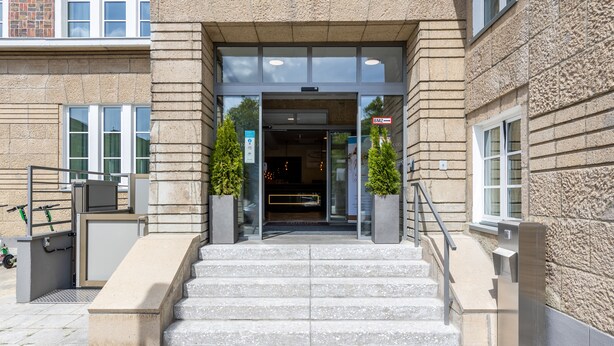A building entrance with a set of stone steps leading up to a glass door. - Trip Inn Living & Suites (Essen)