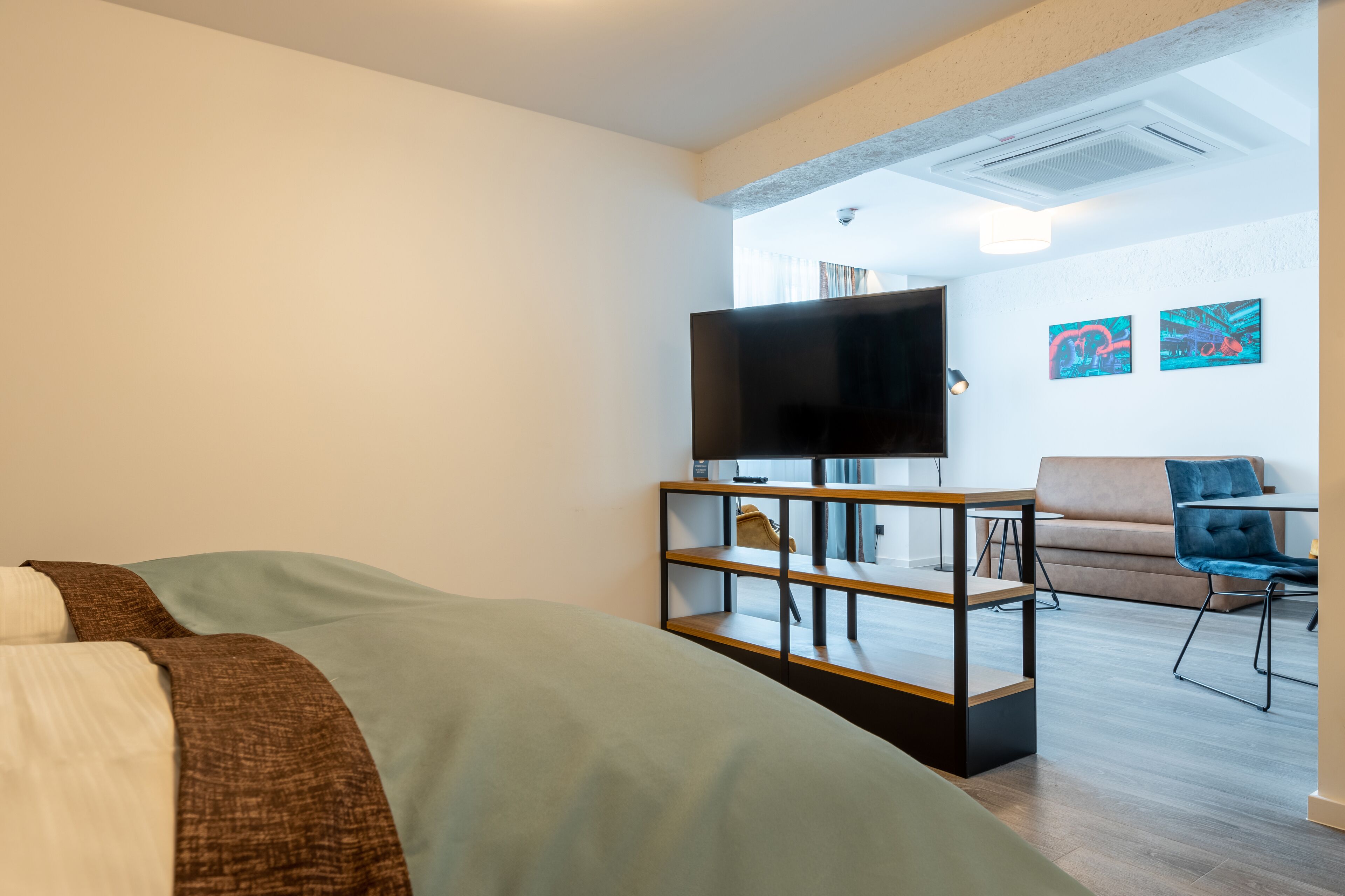 Ein modernes Hotelzimmer mit einem Bett, einem Fernseher auf einem Schrank, einer Couch und einem Sessel.