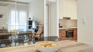 A modern kitchen with wooden cabinets, a built-in oven, and a dining area with a glass table and chairs. - Modern Elegant Apartment at Kolonaki (Athina)