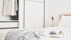 A neatly made bed with a white blanket, a small tray with a glass of water and croissants, and a hanging clothes rack in the background. - Modern Elegant Apartment at Kolonaki (Athina)