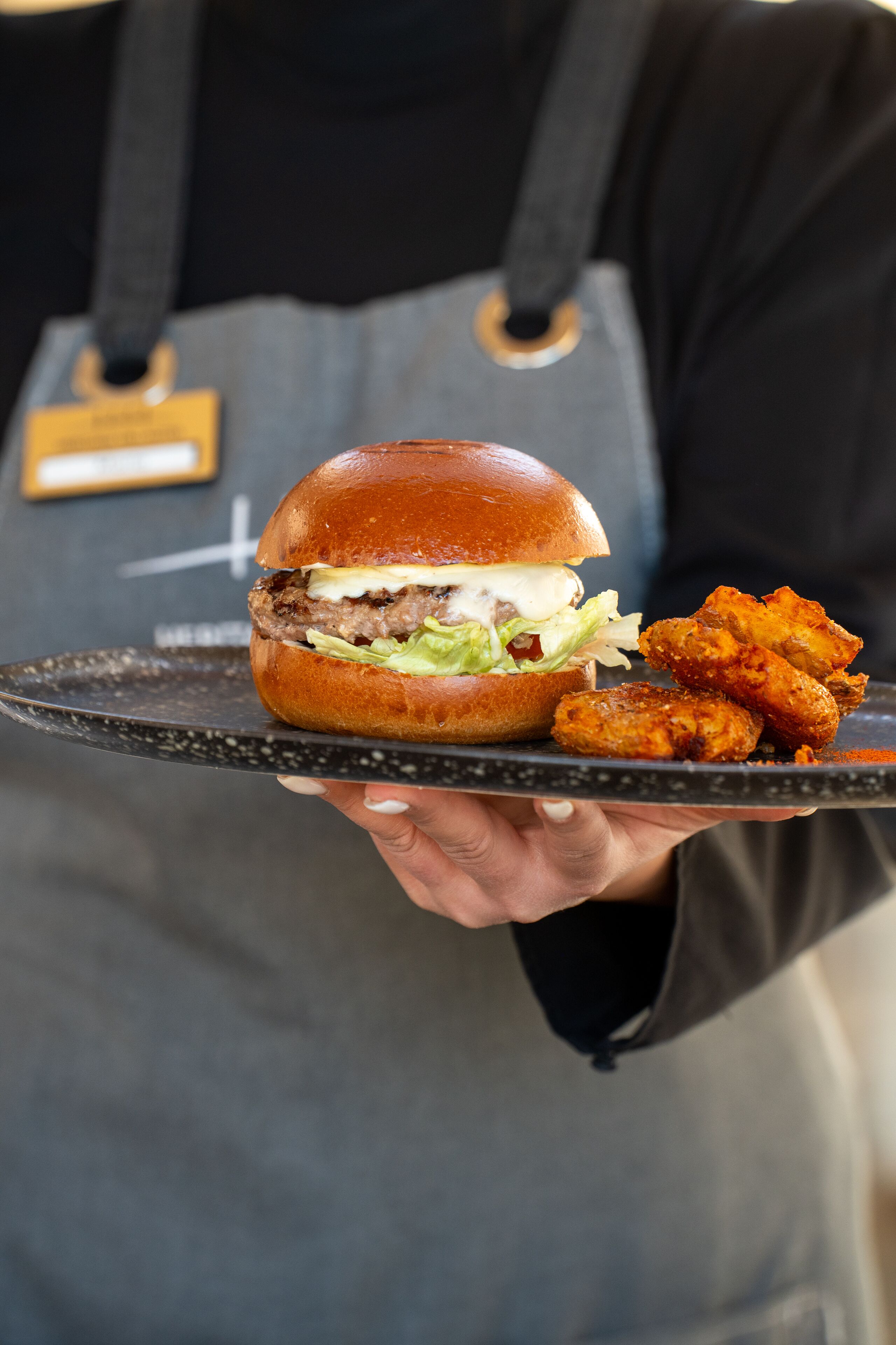 A person holding a tray with a burger and fried items.