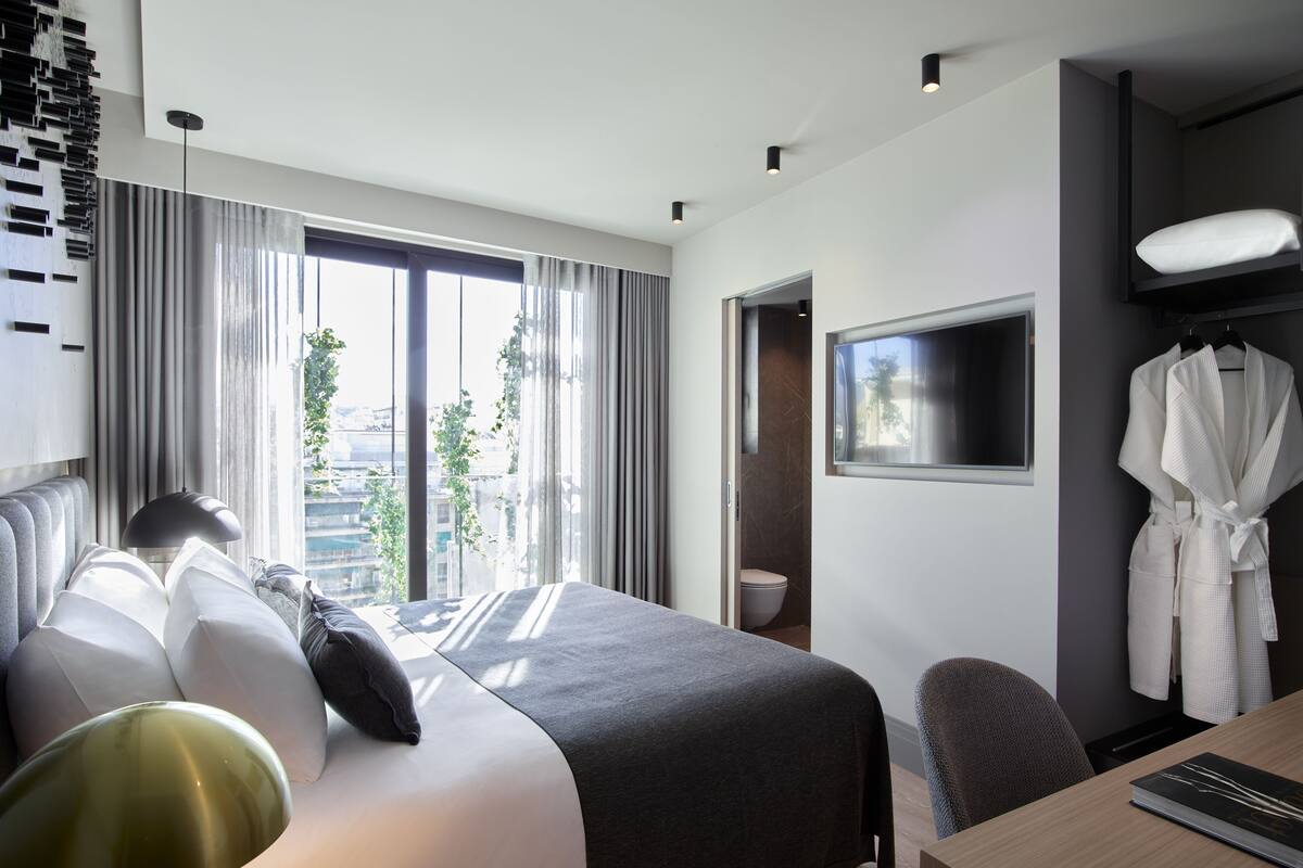A modern hotel room with a large bed, a desk, a robe, and a TV.