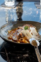 Una ciotola di pasta con carne e verdure su un tavolo di marmo.
