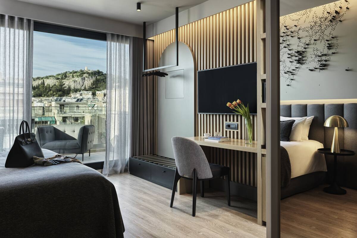 A modern hotel room with a large bed, a desk with a chair, a view of the city, and a large window with curtains.