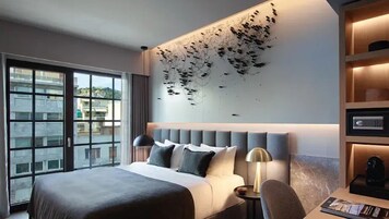 Quarto de hotel moderno com uma cama grande, uma escrivaninha e vista da cidade através de janelas do chão ao teto.