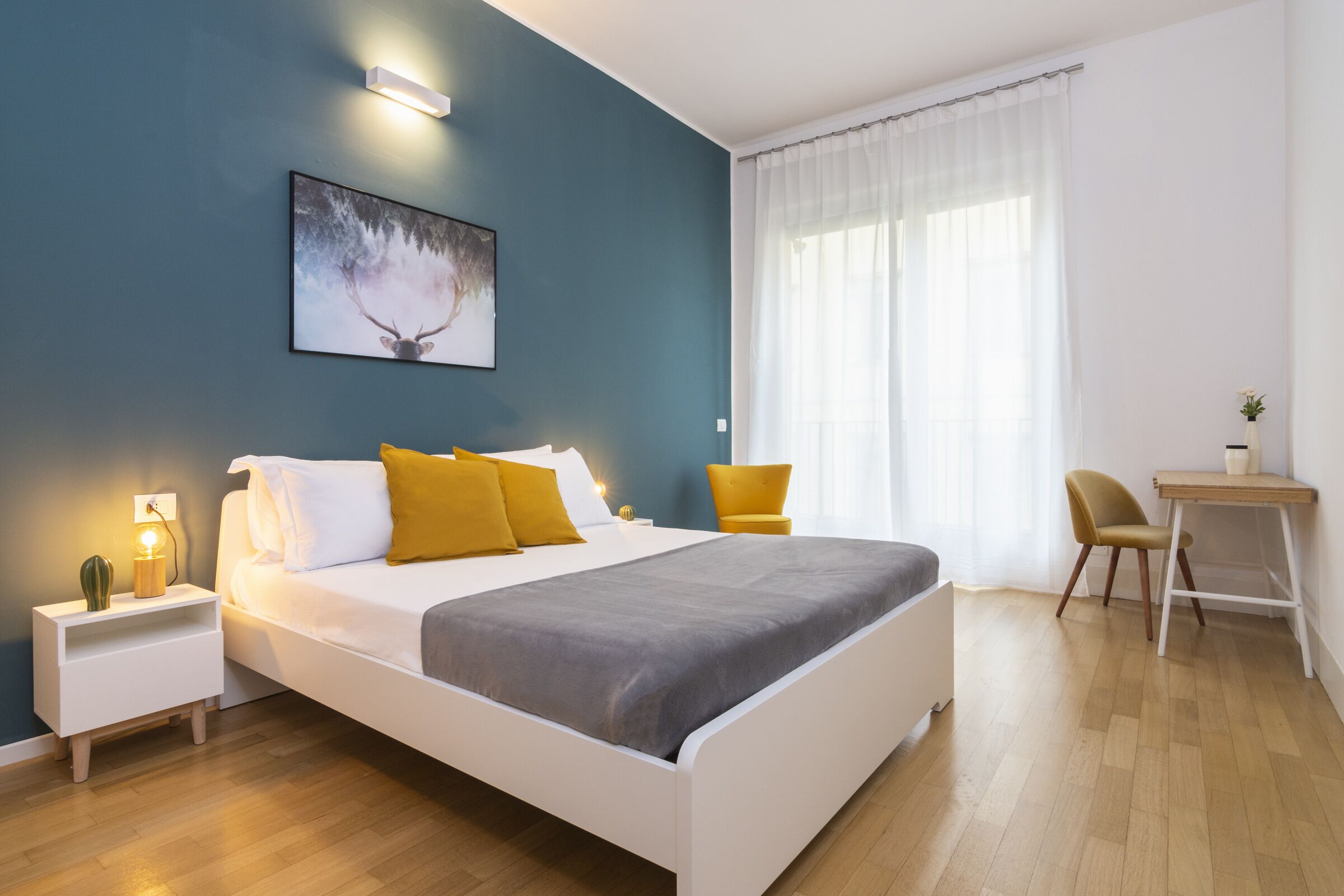 A modern bedroom with a large bed, a nightstand, a desk, and a chair.