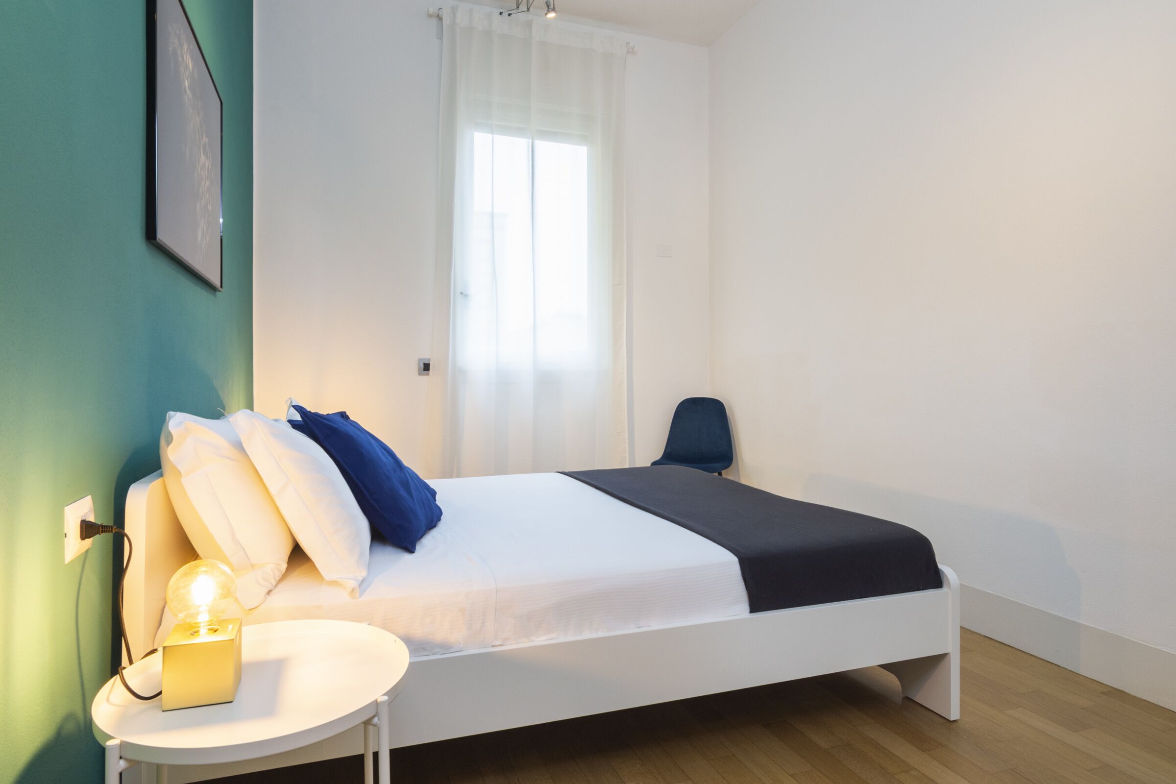 A neatly arranged bedroom with a bed, bedside table, and a window with curtains.