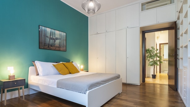 A modern bedroom with a large bed, a nightstand with a lamp, a painting on the wall, and a wardrobe. - Santa Valeria - 4 Bedrooms Apartment (Milan)