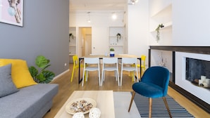 A modern living room with a grey sofa, a blue armchair, and a dining area with white chairs and a wooden table. - Santa Valeria - 4 Bedrooms Apartment (Milan)