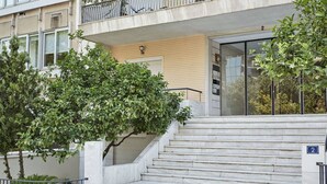 A building entrance with a set of marble stairs leading up to a door, a small tree in front, and a balcony above. - Chic One Bedroom Apartment with Hilton View (Athens)