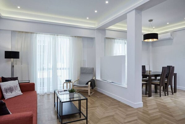 A modern living room with a sofa, a coffee table, a chair, a dining table with chairs, and a TV.