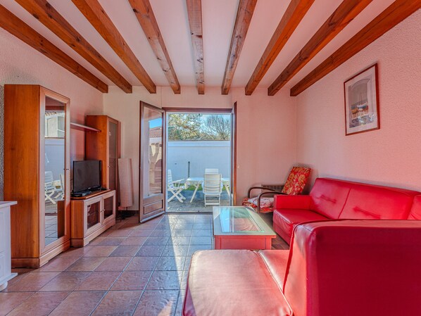 A living room with a red sofa, a television, and a glass coffee table. There is a sliding glass door leading to an outdoor patio with a table and chairs.