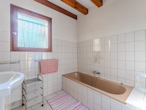 A bathroom with a bathtub, a sink, a window, and a mirror.