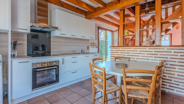 A modern kitchen with white cabinets, a built-in oven, and a dining area with wooden chairs and a table. - Charming 2-BR House with Terrace, Near Beach & Town Center, Sleeps 6 (Biscarrosse Plage)