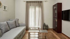 A living room with a sofa, a table, a cabinet, and a TV. - Charming 1bd Apt next to Concert Hall (Athina)