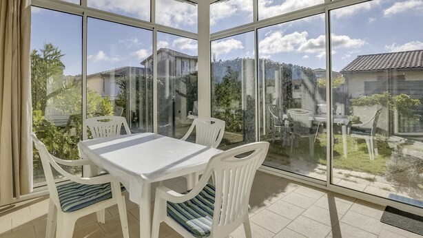 A sunlit room with a large window, a white table, and four white chairs with striped cushions.
