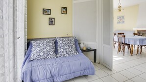 A bedroom with a bed, a small bedside table, and a door leading to a dining area with a table and chairs.
