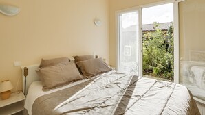 A bedroom with a bed, bedside table, lamp, and a view of a garden through a sliding glass door.
